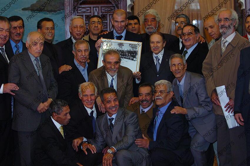 zidane (zinedine) bouteflika (aziz) MAGAZINE ZIDANE EN ALGERIE AVEC LES ANCIENS JOUEURS DE LA PREMIERE EQUIPE DU FLN 1958 ET LE PRESIDENT DE LA REPUBLIQUE D'ALGERIE de g. à dr.: Zouba (abdelhamid) -chemise bleu-,devant lui avec les mains croisés, Kermali (abdelhamid) devant accroupis: Kerroum (abdelkrim), Bekhloufi (kaddour), devant la photo Soukhane (abderahmane), Soukhane (mohamed)-avec ses lunettes- et à sa droite Rouaïr (amar). debout à gauche du président Bouteflika, mekhloufi (rachid) et à sa gauche Maouche (mohamed) 