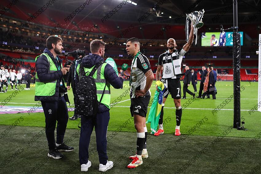 16 March 2025, London - Carabao Cup Final - Liverpool v Newcastle United - Bruno Guimaraes of Newcastle United is interviewed as Joelinton of Newcastle United celebrates with the Carabao Cup trophy - Photo: Jacques Feeney / Offside. FINALE LIVERPOOL-NEWCASTLE (1-2) 